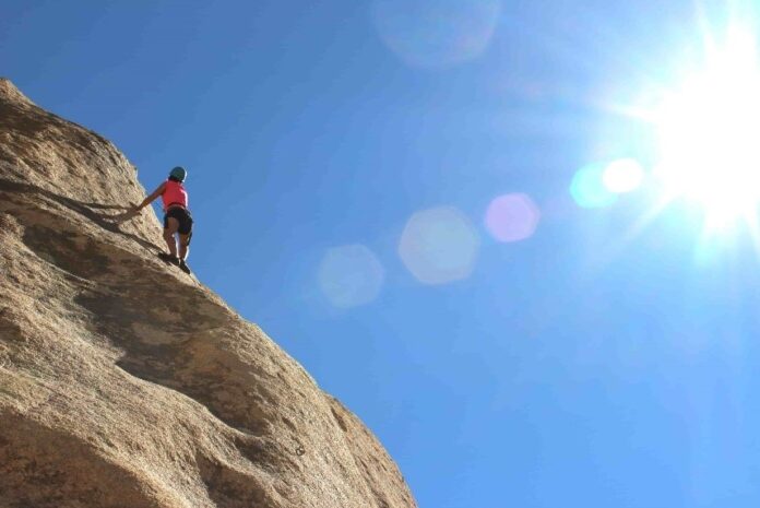 woman climbing rock face with clear blue sky in background