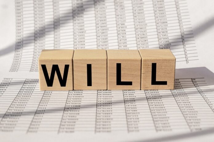 Concept of writing an online Will. Wooden blocks spelling Will, placed across financial documents.