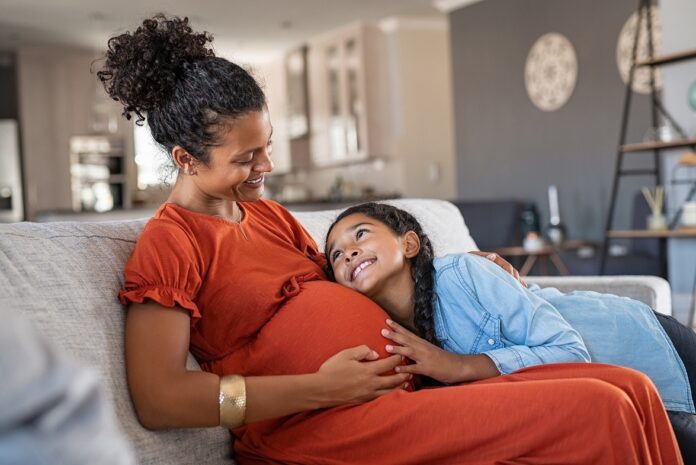 Happy daughter embracing pregnant mother, relaxing together on a sofa